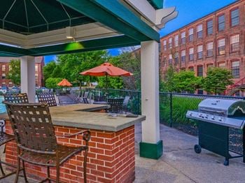 A grill and chairs on a patio with a building in the background